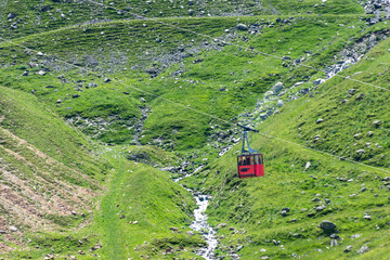 A red cable car descends a grassy slope in a highland meadow
