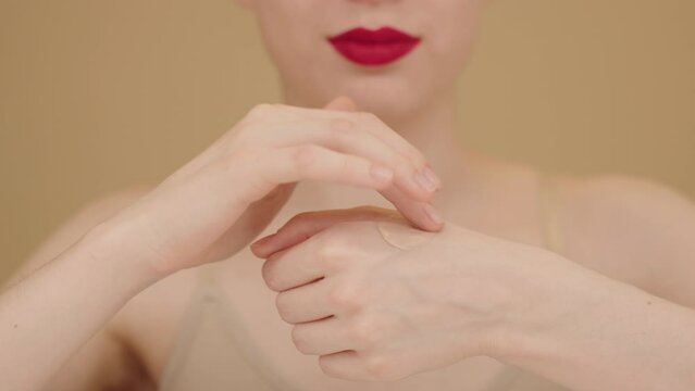 Close-up of female hands of good-looking young woman with smooth skin applying liquid foundation or BB cream on isolated beige background. Advertisement of beauty products, make-up. Slow motion.