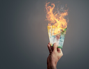 Hand holding burning Swiss franc banknotes showing concept of inflation or money loss