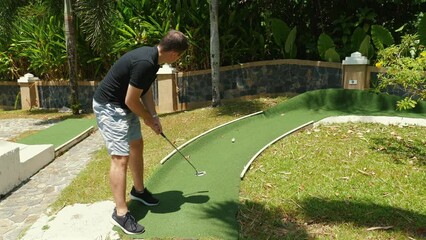 Active adult man playing mini golf on sunny day, enjoying outdoor leisure activities on well-maintained putting green. Outdoor sports and entertainment.