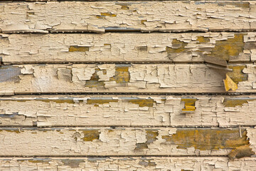 Fragment of the wall of an old wooden building made of horizontal boards. The layer of yellow paint was destroyed and partially crumbled. There are rags hanging. Background. Texture. Grunge.