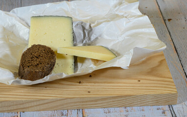 On a light wooden cutting board, a piece of semi-cured Manchego cheese on wax paper, and a sliced piece of rye bread."