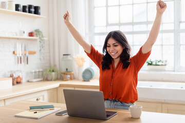Woman celebrating with arms up near laptop