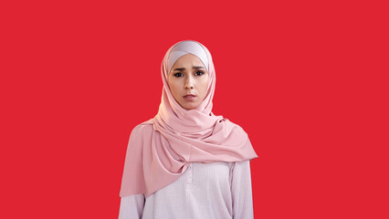 Disturbed woman. Scared face. Stress anxiety. Worried frightened girl in hijab with open mouth isolated on red empty space background.