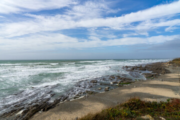 Rochers, sable et algues marrons bordent le littoral atlantique de la baie d'Audierne en Bretagne, sous un ciel couvert, créant une atmosphère mystérieuse.