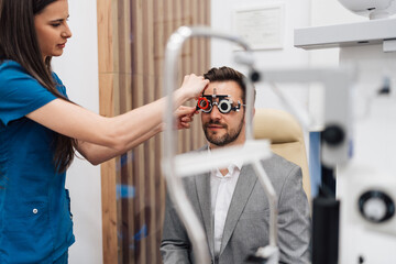 Young female doctor or oculist putting ophthalmic glasses or trial frame on a smiling handsome male...