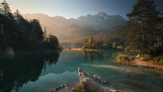 Scenic Lake and mountains lit with warm morning light. Panning shot of a painterly scenery in Bavaria, Germany, with teal calm water and majestic atmosphere