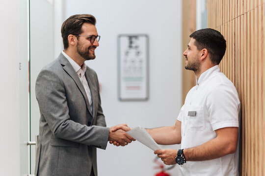 Handsome male patient standing and talking with good looking male doctor in a hall of modern clinic for diagnosis and treatment of eye and sight diseases. Healthcare and medical concept.