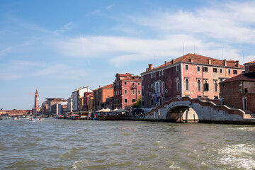 Scenic view from ferry on bridge Dona in Venice, Veneto, Italy, Europe. Summer tourism in Venetian lagoon in Adriatic sea. Timber piles indicating waterways. Famous landmarks in distance