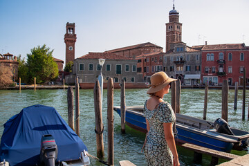 Tourist woman with hat standing next to a water channel on Murano island in city of Venice, Veneto,...