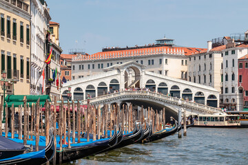 Fototapeta na wymiar Group of gondolas moored in channel Canal Grande with scenic view of famous Rialto bridge in city of Venice, Veneto, Northern Italy, Europe. Venetian architectural landmarks. Romantic vacation