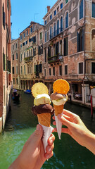 Couple hand holding cones of ice cream with scenic view of water channel in city of Venice, Veneto, Italy, Europe. Local gelato sweet while sightseeing. Urban tourism in summer. Enjoying deserts © Chris