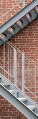 Steel staircase on a brick wall. Two flights of stairs and a red brick wall. Fixed fire escape from the end of the building.