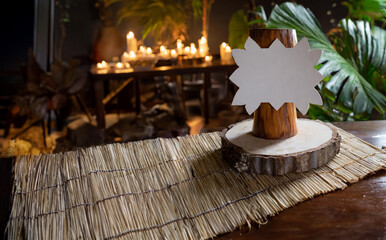 A tropical table topper; table tent with a carved wood frame menu or cocktail list, blank space for custom message or design. Island, glowing candles in the background - jungle hotel
