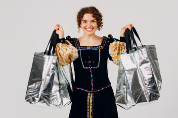 Young adult smiling woman dressed in a medieval dress holding shopping bags in hands isolated white background