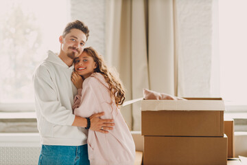 Happy young family couple man and woman hugging after moving cardboard boxes to their new apartment.