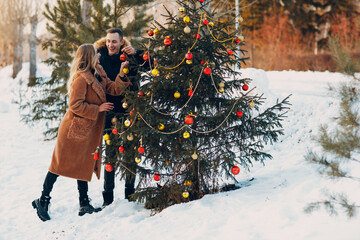 Young adult couple decorates christmas tree in winter forest. New year pine holiday party celebration concept