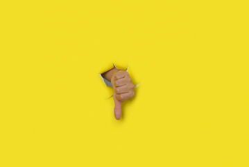 Female hand with thumb down as a sign of disapproval, coming out of the hole of a yellow torn paper...
