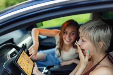 Happy young two women driver tourist travelers with digital tablet USA American map at rental car...