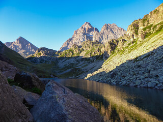 Fototapeta premium Scenic sunrise view of mountain summit Monte Viso (Monviso) and lake Lago Grande di Viso in the Cottian Alps, Piemonte, Italy, Europe. Rock walls of Stone king are shining in warm red orange colors