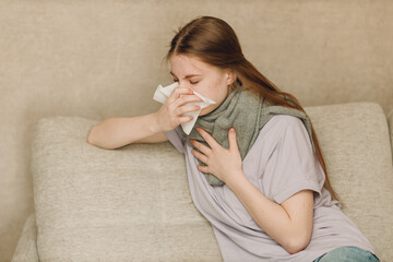 Young woman wearing scarf has flu ill sick disease cold at home indoor on sofa with napkins