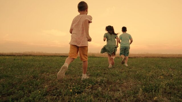 Happy boy, girl run in field, playing in nature. Happy childhood. Family, weekend outdoors. Teenagers play running, Funny children play in park, friends run in summer. Child run on grass, sunset