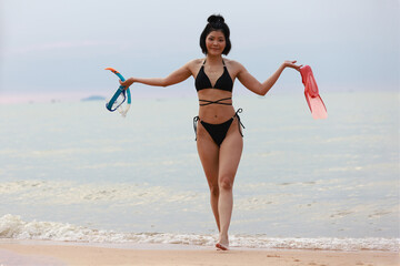 A Young Asia woman with a swimming suit holds a snorkel and fins, Happy summer vacation on a tropical beach