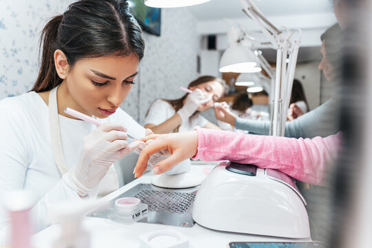 Professional manicurists working in a modern beauty salon. Satisfied female clients receiving nail manicure treatments at spa center.