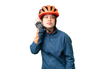 Young cyclist girl over isolated chroma key background listening to something by putting hand on the ear