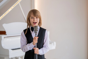 A boy in a black vest and bow tie sings into a microphone.