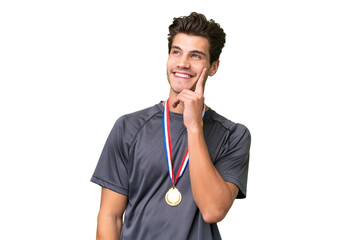 Young caucasian man with medals over isolated background thinking an idea while looking up