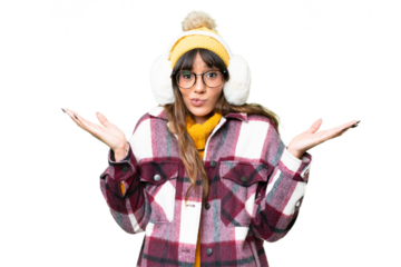 Young caucasian woman wearing winter muffs over isolated chroma key background having doubts while raising hands