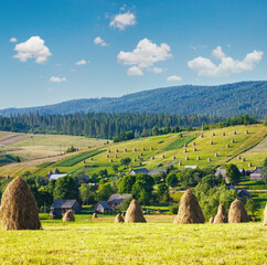 Summer mountain village outskirts with haystacks on field (Carpathian, Ukraine)