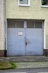 Altes blaues Garagentor aus Holz vor einer Einfahrt, mit senkrechten Streben und Glasfenstern in...