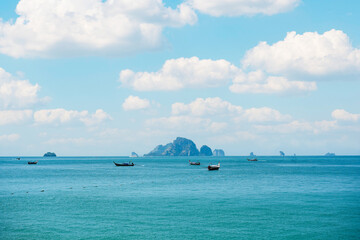 Fisherman parking traditional long tail fishing boats in sea coast with rock mountain against blue sky with cloud at Ao Nang Beach - Krabi, Thailand.