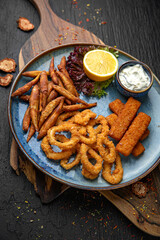 A plate of small deep-fried fish, squid rings and fish sticks.  Menu for a pub on a dark background. Colorful juicy food photography.