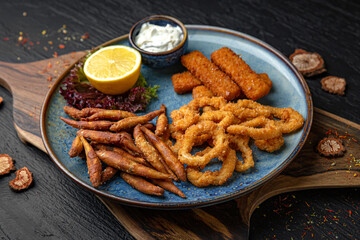 A plate of small deep-fried fish, squid rings and fish sticks.  Menu for a pub on a dark background. Colorful juicy food photography.
