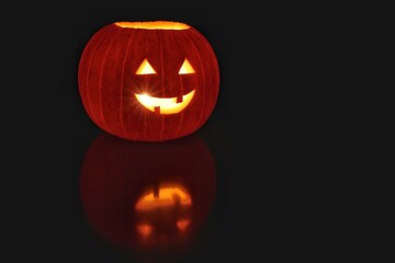 Nightshot of a Halloween pumpkin with a friendly face and a reflection with a meaner looking face....