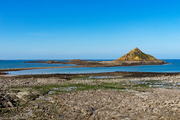 L'îlot du Verdelet, accessible à marée basse, sous un ciel bleu dans les Côtes d'Armor, Bretagne.