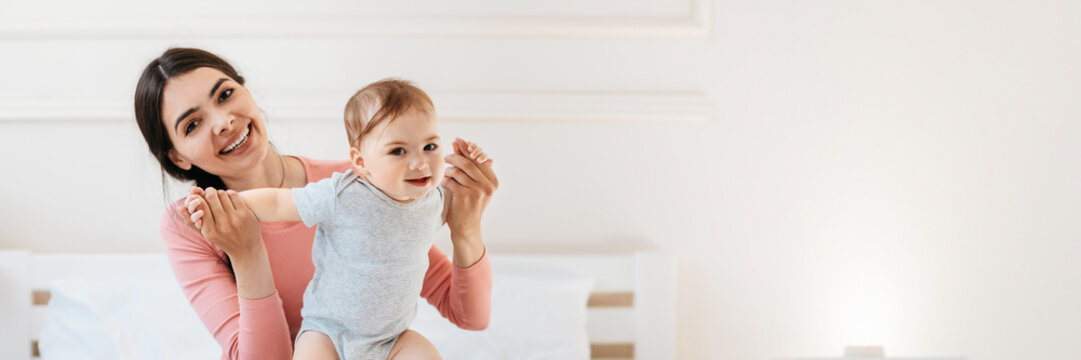 Happy mom helping to her infant child making first steps