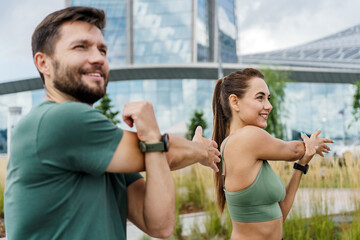 Energetic couple stretches outdoors with cityscape background, promoting health and teamwork.