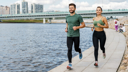 Motivated couple jogs by the river, blending fitness with the scenic beauty of the cityscape.
