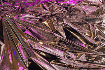 a close up of a pile of crumpled aluminum foil with purple lights behind it