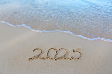 New Year 2025 handwritten in the white sand surface.