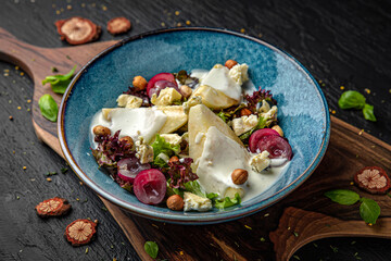 Warm salad with baked pear, melted brie and dorblu cheese, grapes, nuts and herbs. Menu for a pub on a dark background. Colorful juicy food photography.