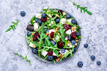 Healthy useful salad with beetroot, blueberries, feta cheese, arugula and walnuts, gray table background, top view - 791031420
