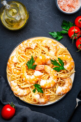 Ready for eat pasta with shrimp, olive oil and parsley on black table background. Top view