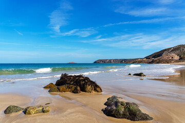 Fototapeta na wymiar Sur la plage de la Fosse, Côtes d'Armor, sous le soleil éclatant, le sable est parsemé de quelques rochers, tandis qu'une belle vague déferle majestueusement.