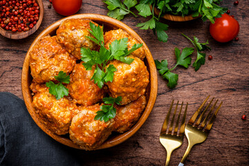 Meatballs with tomato sauce and parsley in bowl on rustic wooden table background. Top view