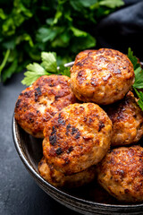 Homemade meatballs with spices and parsley in ceramic bowl, black table background, top view